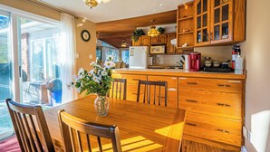 Una cocina con armarios de madera, una mesa de comedor con sillas, un refrigerador y una cafetera.