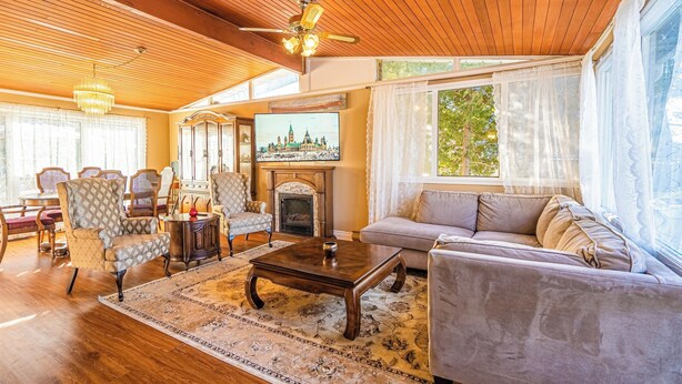 Un salón comedor amplio con suelo de madera, una chimenea y un ventanal con cortinas ligeras.