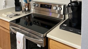 Cozinha com armários de madeira, micro-ondas de aço inoxidável, forno, máquina de café e um conjunto de facas.