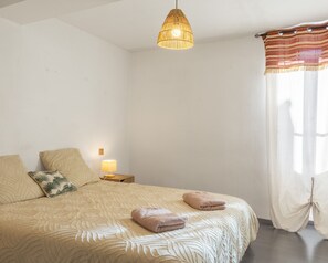 A bedroom with a bed, a bedside lamp, a hanging light fixture, and a window with curtains.