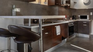 A modern kitchen with stainless steel appliances, a bar area, and a clock on the wall. - Apartment 'La Glycine' with Wi-Fi and Air Conditioning (Montolieu)