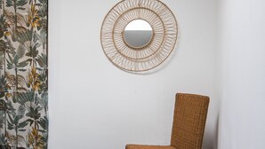 A room with a wicker chair, a wall-mounted mirror, and a floral-patterned curtain. - Apartment 'La Glycine' with Wi-Fi and Air Conditioning (Montolieu)