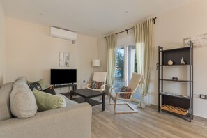 Un salon comprenant un canapé, une table basse, un téléviseur, deux fauteuils, une bibliothèque et une fenêtre avec des rideaux.