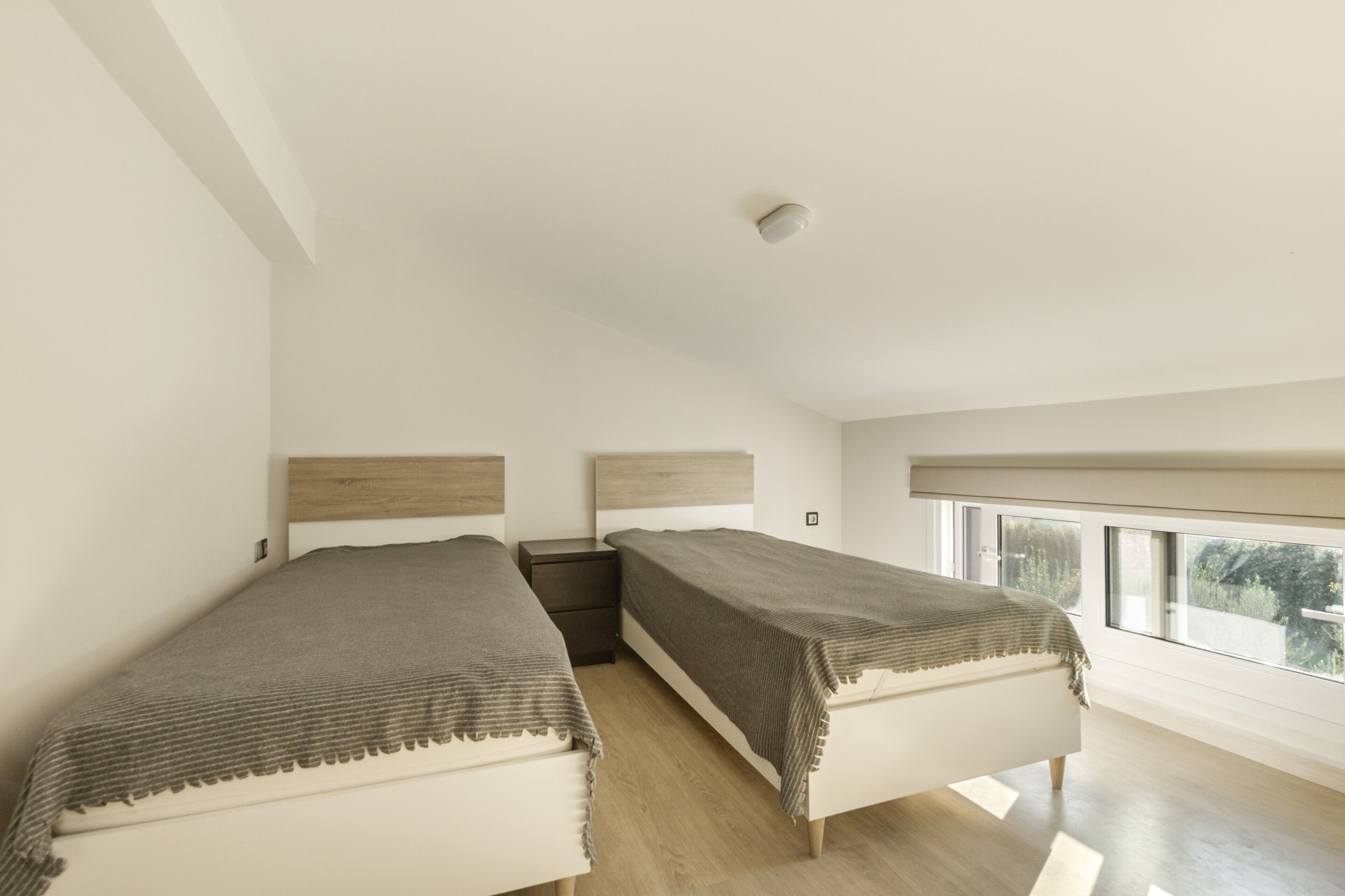 Camera da letto con due letti, un comodino, una finestra e una luce a soffitto.
