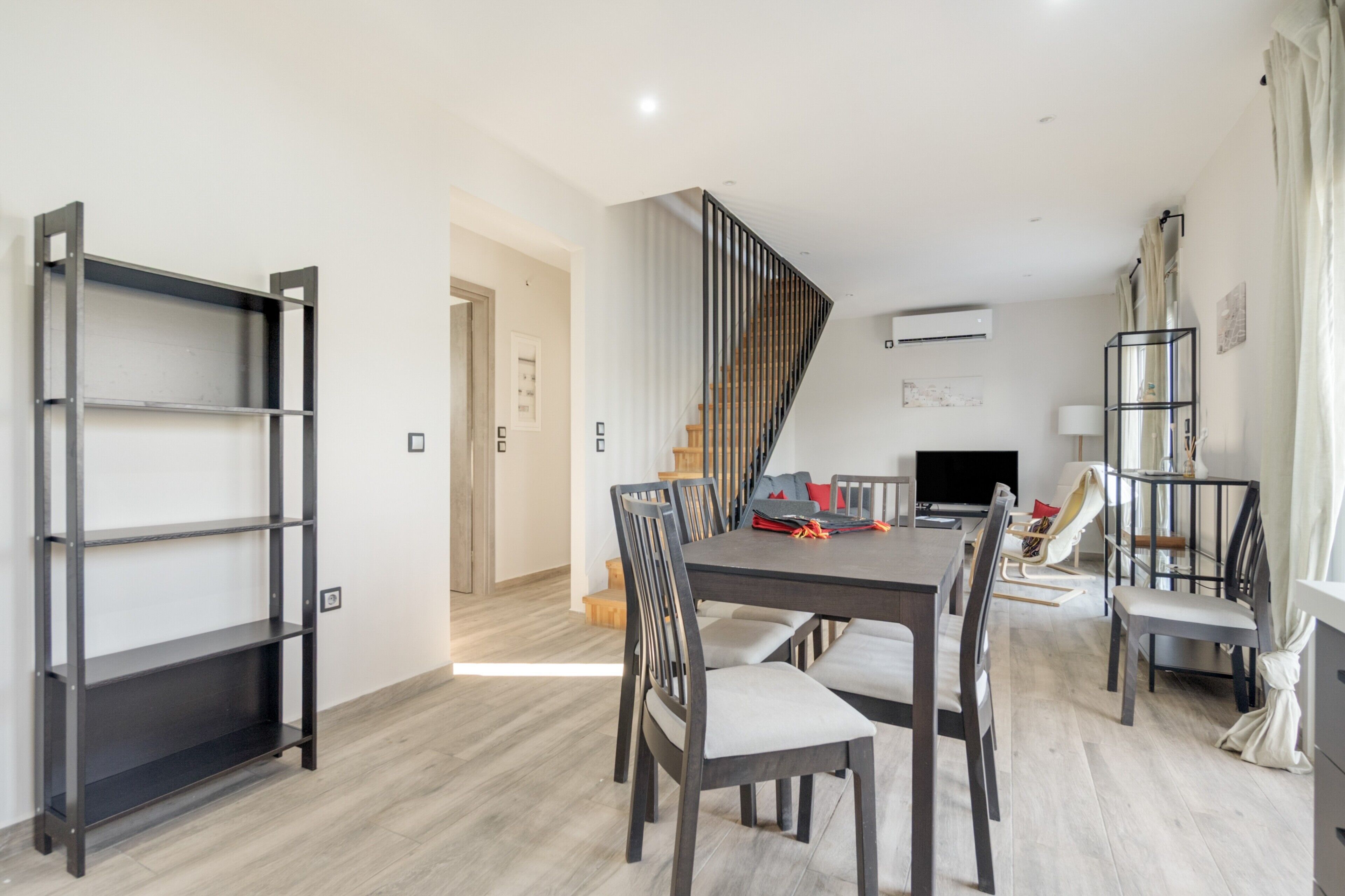 A modern dining area with a wooden table, chairs, and a black metal shelf unit.