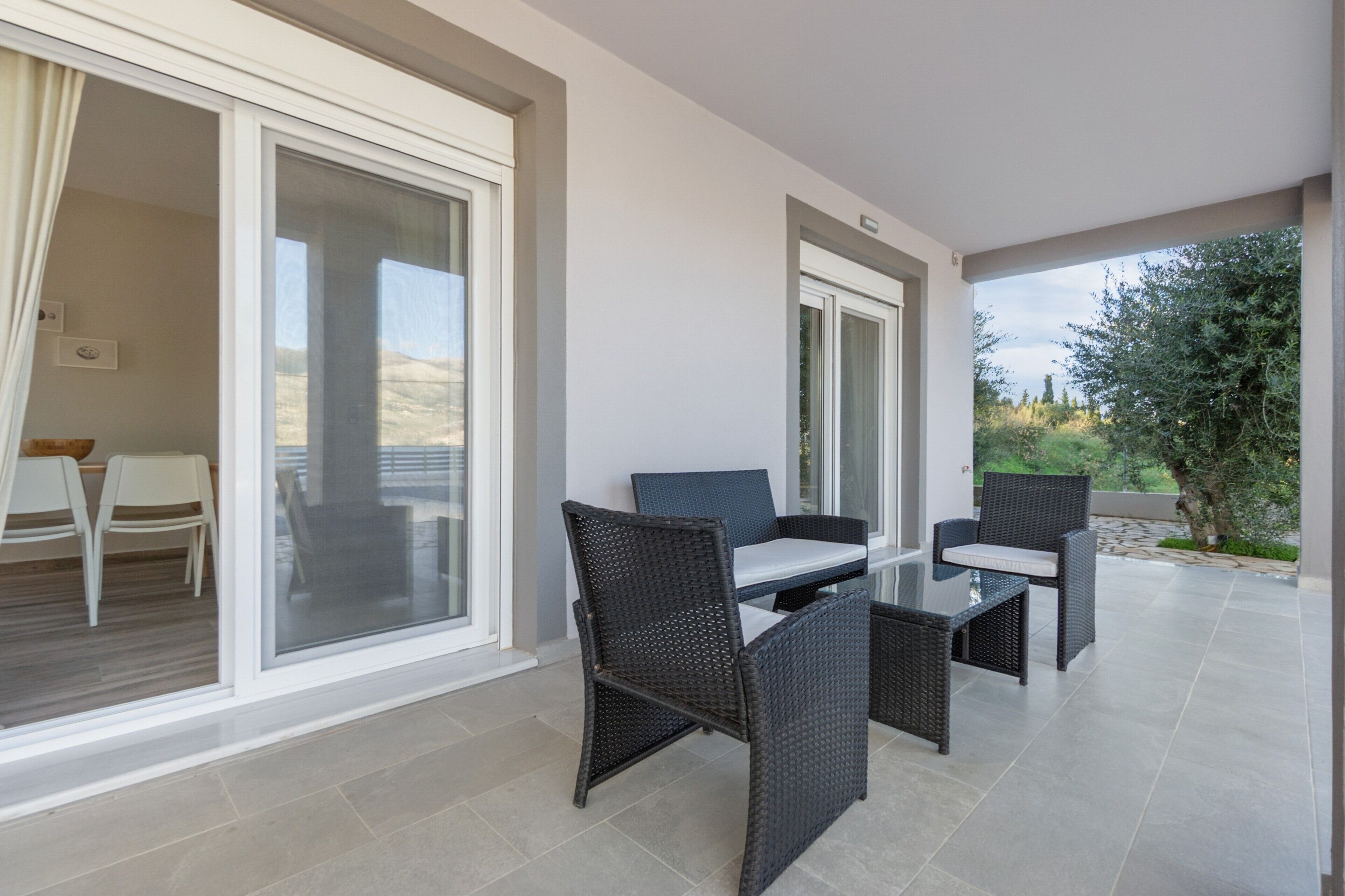 Ein Balkon mit Korbmöbeln, einer Glastür und Blick ins Grüne.