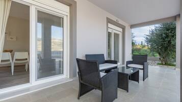 Ein Balkon mit Korbmöbeln, einer Glastür und Blick ins Grüne.