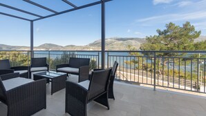 Un área de estar al aire libre techada, con mobiliario de mimbre y vista a un lago y montañas.