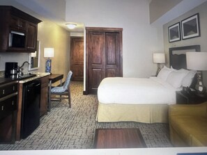 Una habitación de hotel con cama, escritorio, silla, cafetera y lámpara.
