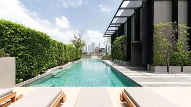 Un espace piscine moderne avec des chaises longues, une piscine à eau claire et, en arrière-plan, la vue sur les gratte-ciel de la ville.