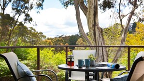 Un balcon avec une table, des chaises, une cafetière, une tasse et une petite plante.