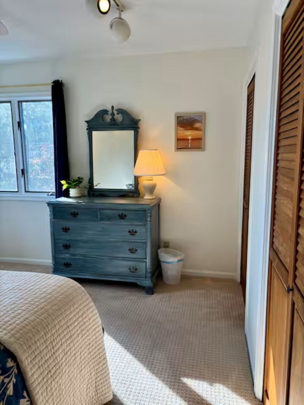 A bedroom with a bed, a dresser, a lamp, a window, and a picture on the wall.