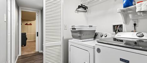 A laundry room with a Maytag washer and dryer, a drying rack, and a shelf with cleaning supplies.