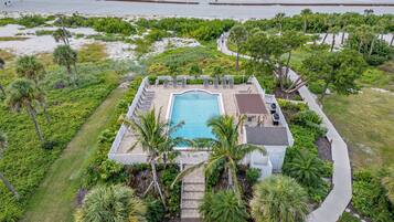 An aerial view of a resort with a swimming pool surrounded by palm trees and a beach.