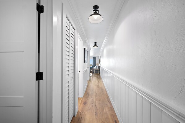 A hallway with white walls, wooden flooring, and a ceiling light fixture. - Captiva Beachfront Front Condo| Heated Pool| Golf Cart (Captiva Island)