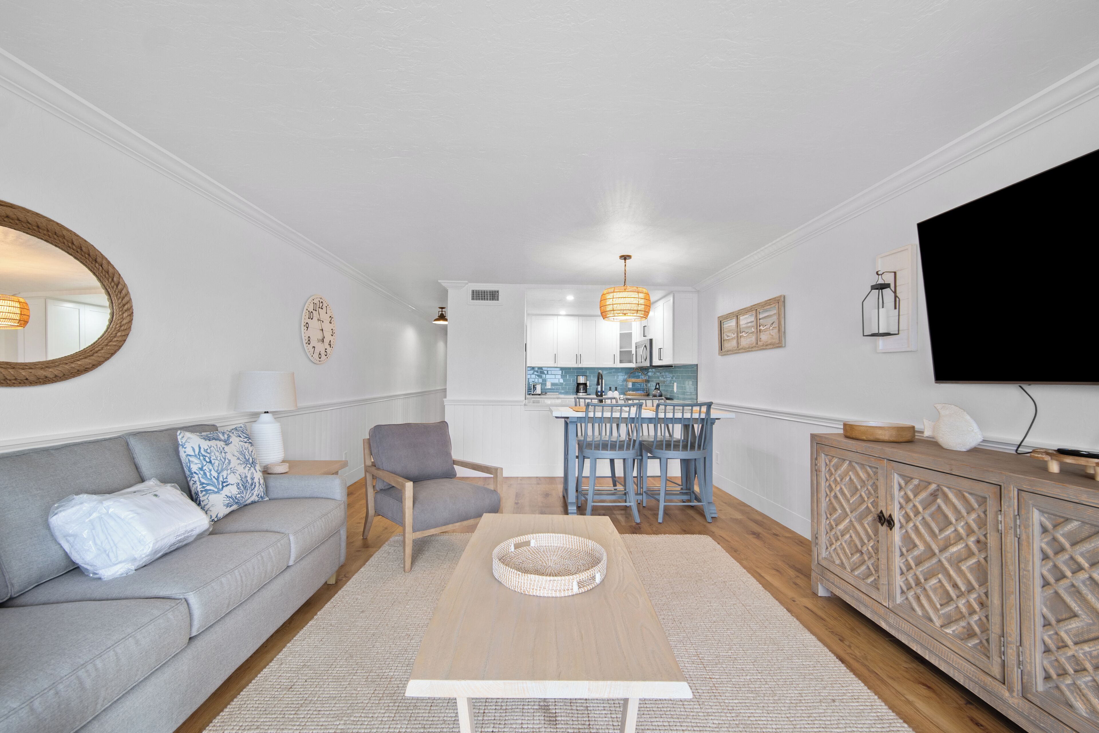 Un salon moderne avec un canapé gris, une table basse en bois et une cuisine en arrière-plan.