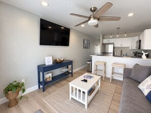 A modern living room with a television, a ceiling fan, a white coffee table, and a grey sofa.