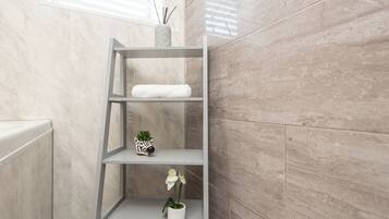 A bathroom with a marble wall, a white radiator, and a grey shelf with a white towel, a small plant, and a decorative item.