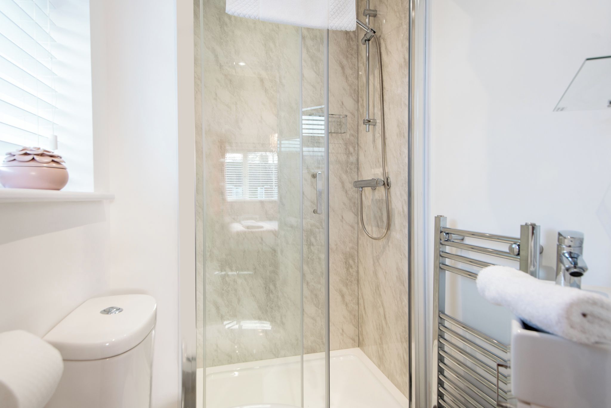 A modern bathroom with a glass-enclosed shower, a toilet, and a towel rack.