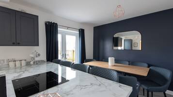A modern kitchen with a marble countertop, dark blue upholstered chairs, and a wooden dining table.