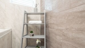 Un baño con pared de mármol, un radiador blanco y un estante gris con una toalla blanca, una planta pequeña y un adorno.