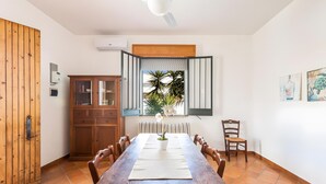 Ein Essbereich mit Holztisch, Stühlen, einem Schrank und einem Fenster mit Blick auf Palmen.
