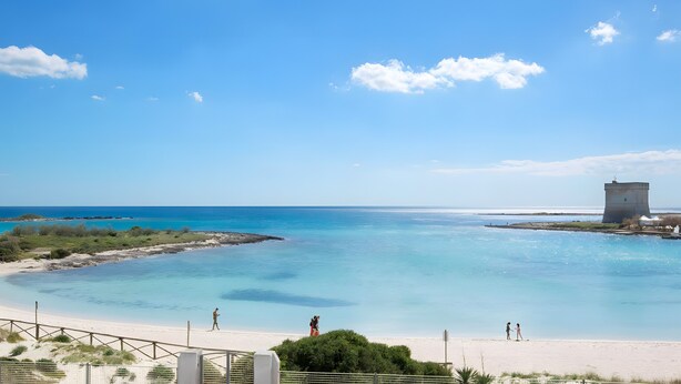 Ein Strand mit klarem, blauem Wasser, einem Sandufer und einem historischen Turmgebäude.