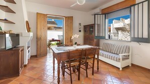 Ein Essbereich mit Holztisch und -stühlen, einem weißen Sofa, einem Deckenventilator und Blick durch ein Fenster.