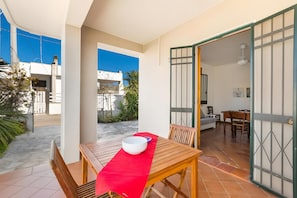 An open patio with a wooden table and chairs, a red table runner, and a view of the street and buildings in the background.
