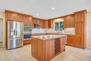 A kitchen with wooden cabinets, stainless steel appliances, a granite countertop, and a window with a view of trees.