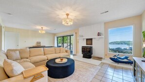 Ein Wohnzimmer mit Sofa, Hocker, Kamin und großen Fenstern mit Aussicht.
