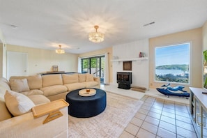 A living room with a sofa, ottoman, fireplace, and large windows with a view.