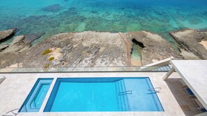 A clear blue pool with a view of the ocean and rocky terrain. - SeaDreams 6: Oceanfront Condos w/Pool, Hot Tub, & Rooftop Patio (West Bay)