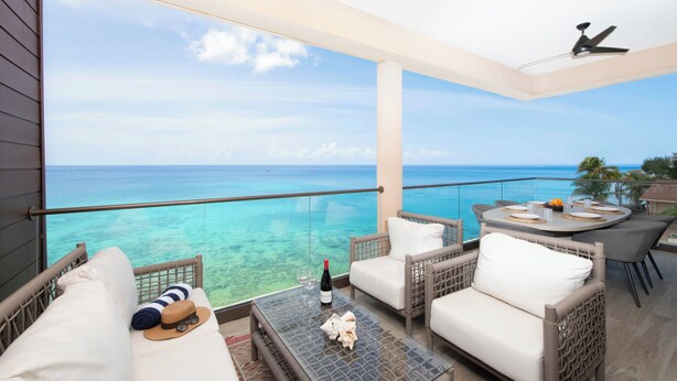 A balcony with wicker furniture, a glass table, and a view of the ocean. - SeaDreams 6: Oceanfront Condos w/Pool, Hot Tub, & Rooftop Patio (West Bay)