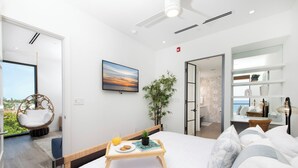 A modern bedroom with a bed, bedside table, and a view of the outdoors. - SeaDreams 6: Oceanfront Condos w/Pool, Hot Tub, & Rooftop Patio (West Bay)