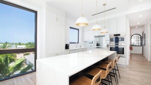 A modern kitchen with a large island, pendant lights, and a view of the outdoors. - SeaDreams 6: Oceanfront Condos w/Pool, Hot Tub, & Rooftop Patio (West Bay)