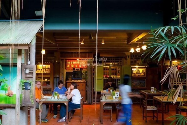 An outdoor dining area with tables and chairs, a wooden structure, and hanging plants. - DaDa97 Hostel (Bangkok)