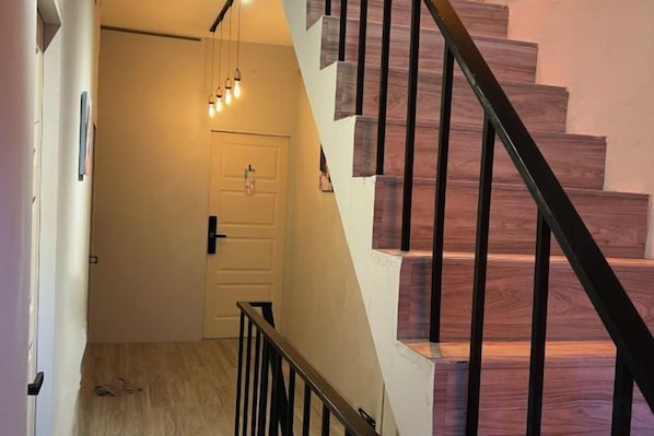 A staircase with wooden steps and a black handrail, leading to a white door with a light switch above it. - DaDa97 Hostel (Bangkok)