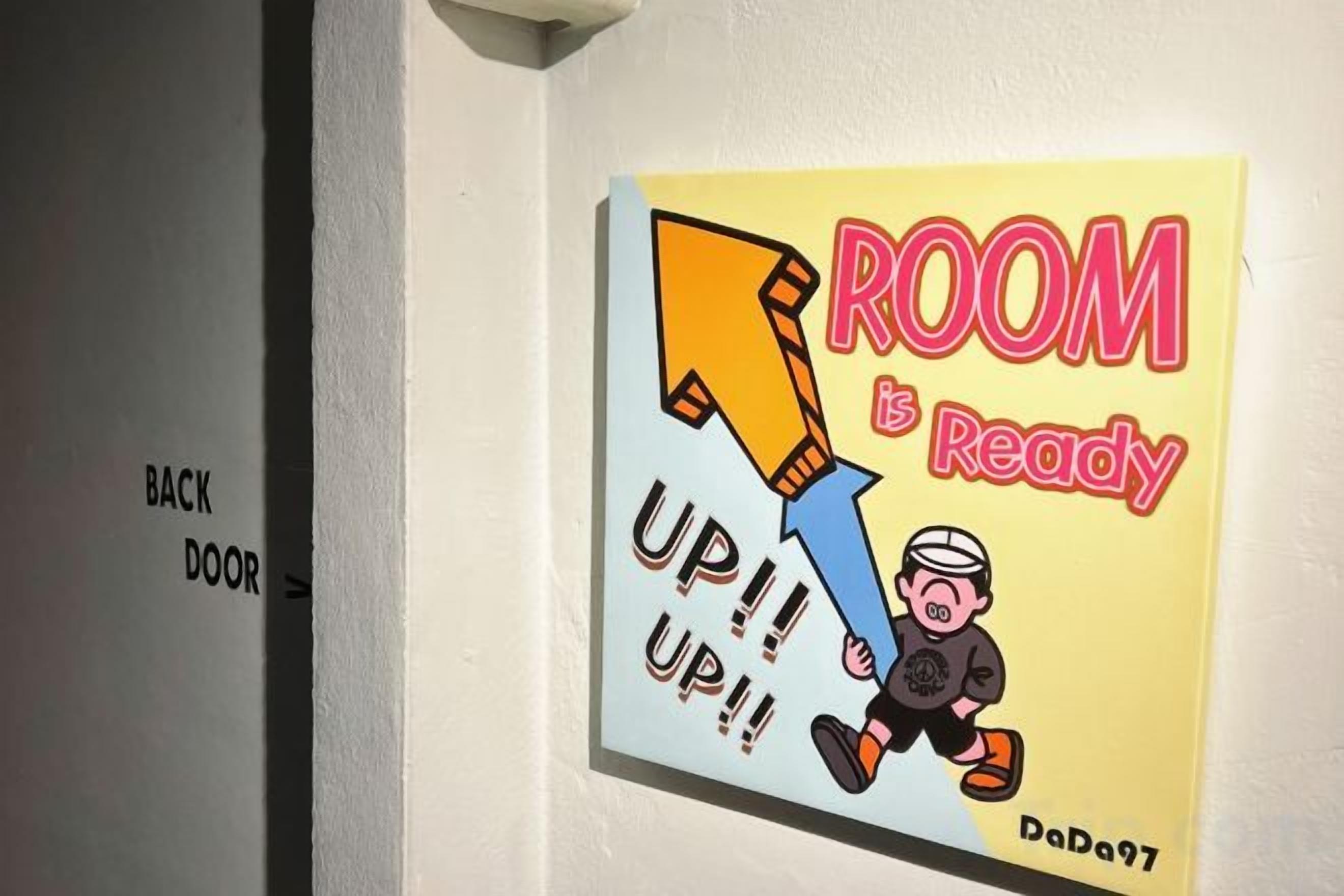 A wall with a sign that reads 'ROOM is Ready' and 'UP!! UP!!' with a cartoon character.