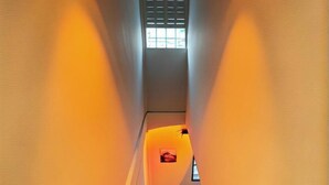 Un corridoio stretto con un soffitto spiovente e una piccola finestra in fondo.