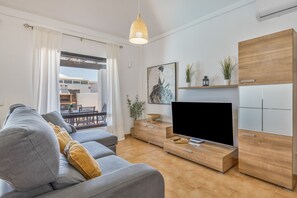 A modern living room with a sofa, TV, wooden cabinet, and a dining area visible through a glass door. - Holiday Villa 'Vera' with Mountain Views, Private Pool, and Wi-Fi (Playa Blanca)
