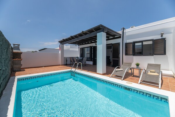 A rooftop pool with a pergola, lounge chairs, and a view of the city.