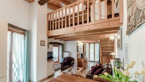A spacious living area with a wooden dining table, a sofa, and a staircase leading to an upper level. - Two-room apartment in the valleys of Capriasca (Ca' del Primo) (Odogno)