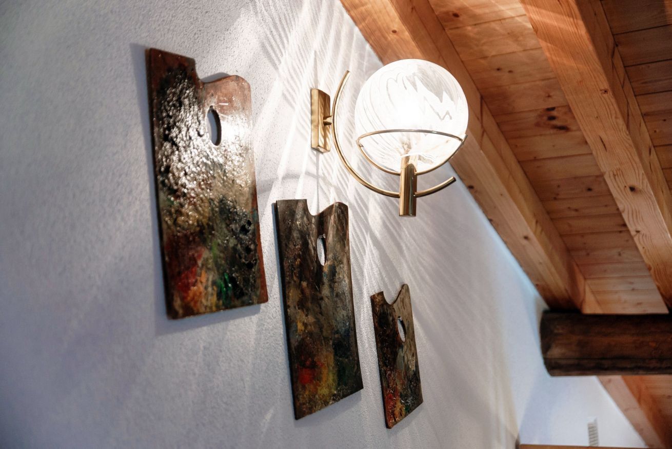 Un mur orné de trois œuvres d’art en métal et d’un luminaire fixé au mur.