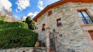 A stone building with a wooden roof, a metal gate, and a staircase leading to the entrance. - Two-room apartment in the valleys of Capriasca (Ca' del Primo) (Odogno)
