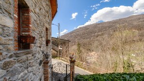 A stone building with a metal gate, a brick window, and a view of a hilly landscape. - Two-room apartment in the valleys of Capriasca (Ca' del Primo) (Odogno)