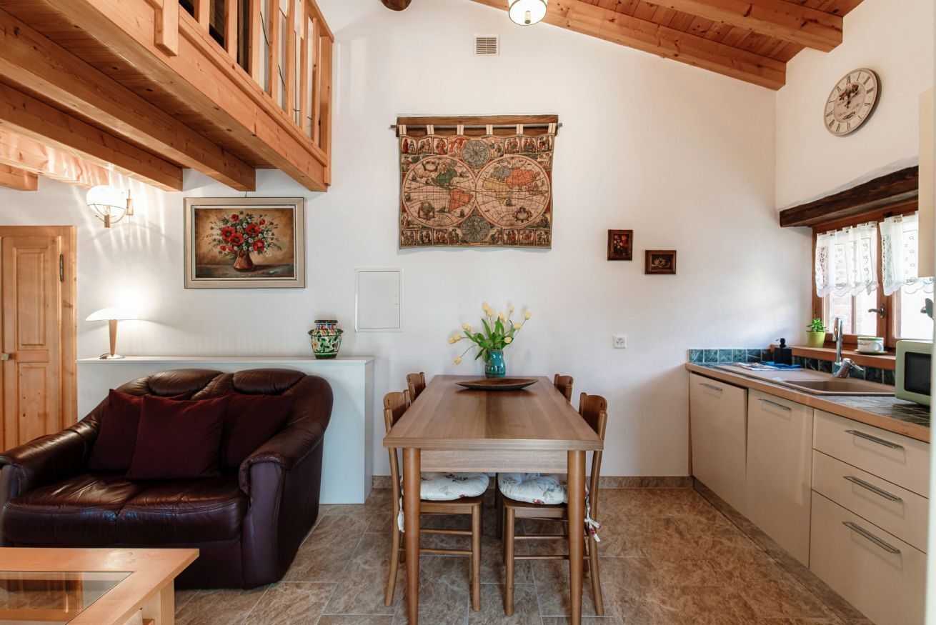 A cozy living room with a leather sofa, wooden dining table, and a kitchen area with a sink and cabinets.