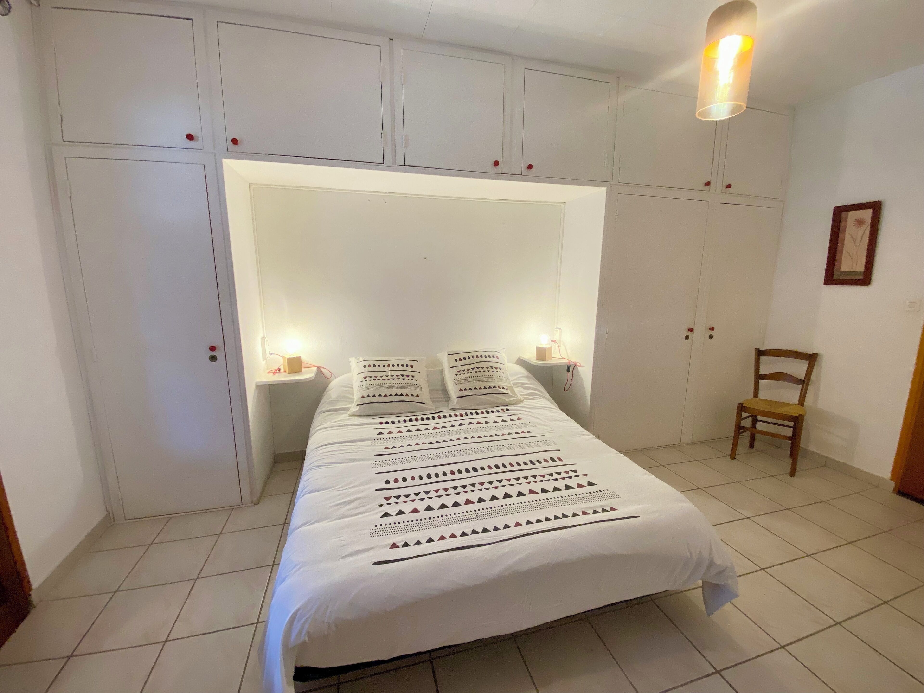 Ein Schlafzimmer mit einem großen Bett, weißen Wänden und einer Deckenleuchte.