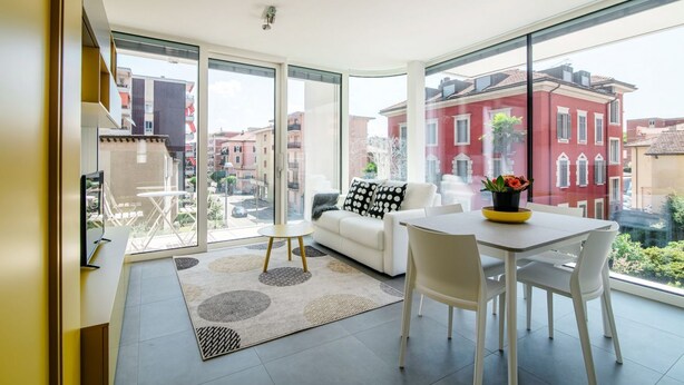 A modern living room with a large glass door leading to a balcony, a white sofa, a dining table with chairs, and a small side table. - A one-bedroom apartment for an excellent stay (FLAT IRON 7) (Viganello)