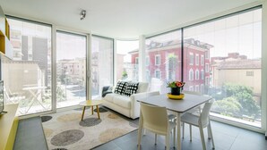 A modern living room with a large sliding glass door leading to a balcony, a white sofa, a dining table with chairs, and a small round table with a chair. - A one-bedroom apartment for an excellent stay (FLAT IRON 7) (Viganello)